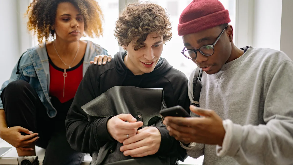 Three friends looking at a smartphone together while making social plans.