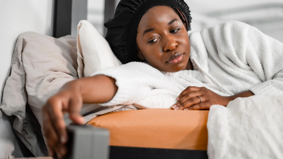 Person reaching for an alarm clock in bed in the morning