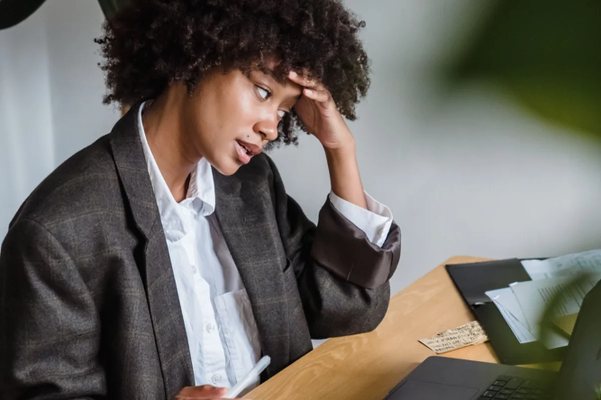 A stressed person sitting at a desk with notes and a laptop.