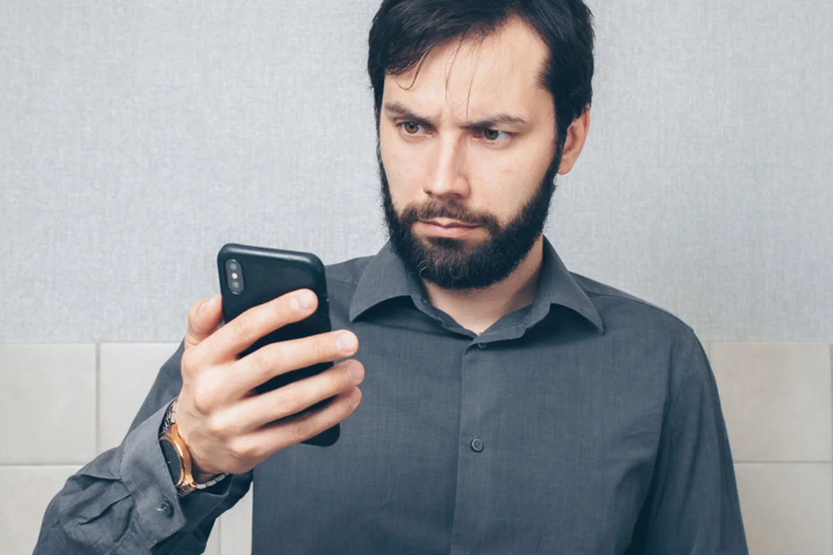 A worried person looking at a phone with a tense expression.