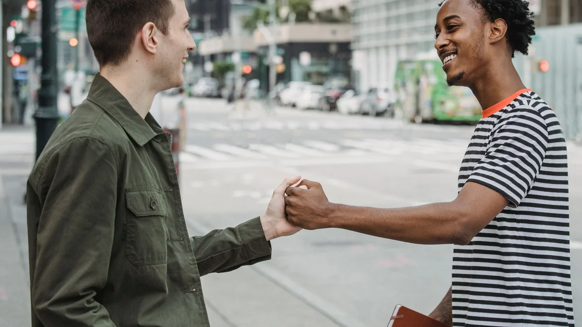 Two young friends greeting each other warmly on a city street.