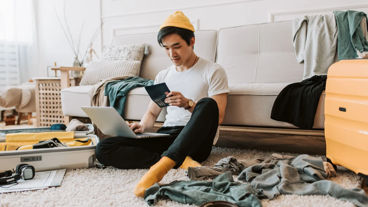 Man sitting in a messy living room surrounded by clothes and luggage