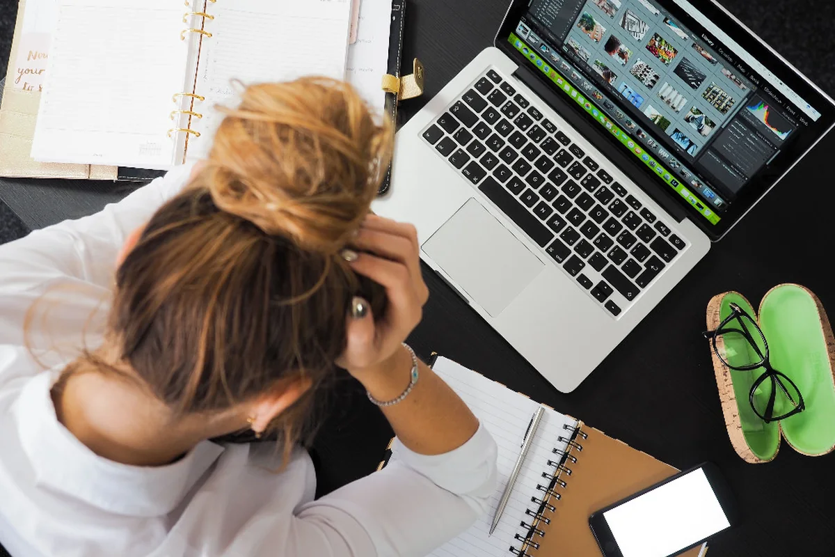 Overhead view of a stressed person with a laptop, phone and notes.