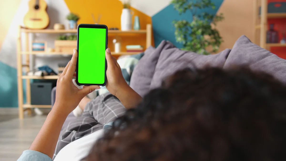 A person relaxing at home on a couch while checking a smartphone.