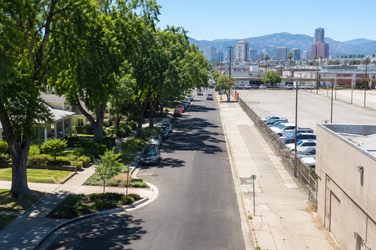 Tree-lined residential neighborhood beside a heavily paved urban area with little shade