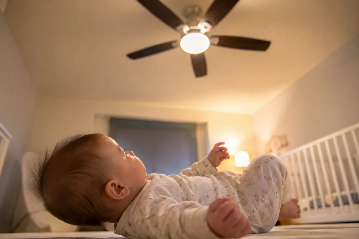 Baby lying down in a nursery while watching a ceiling fan overhead