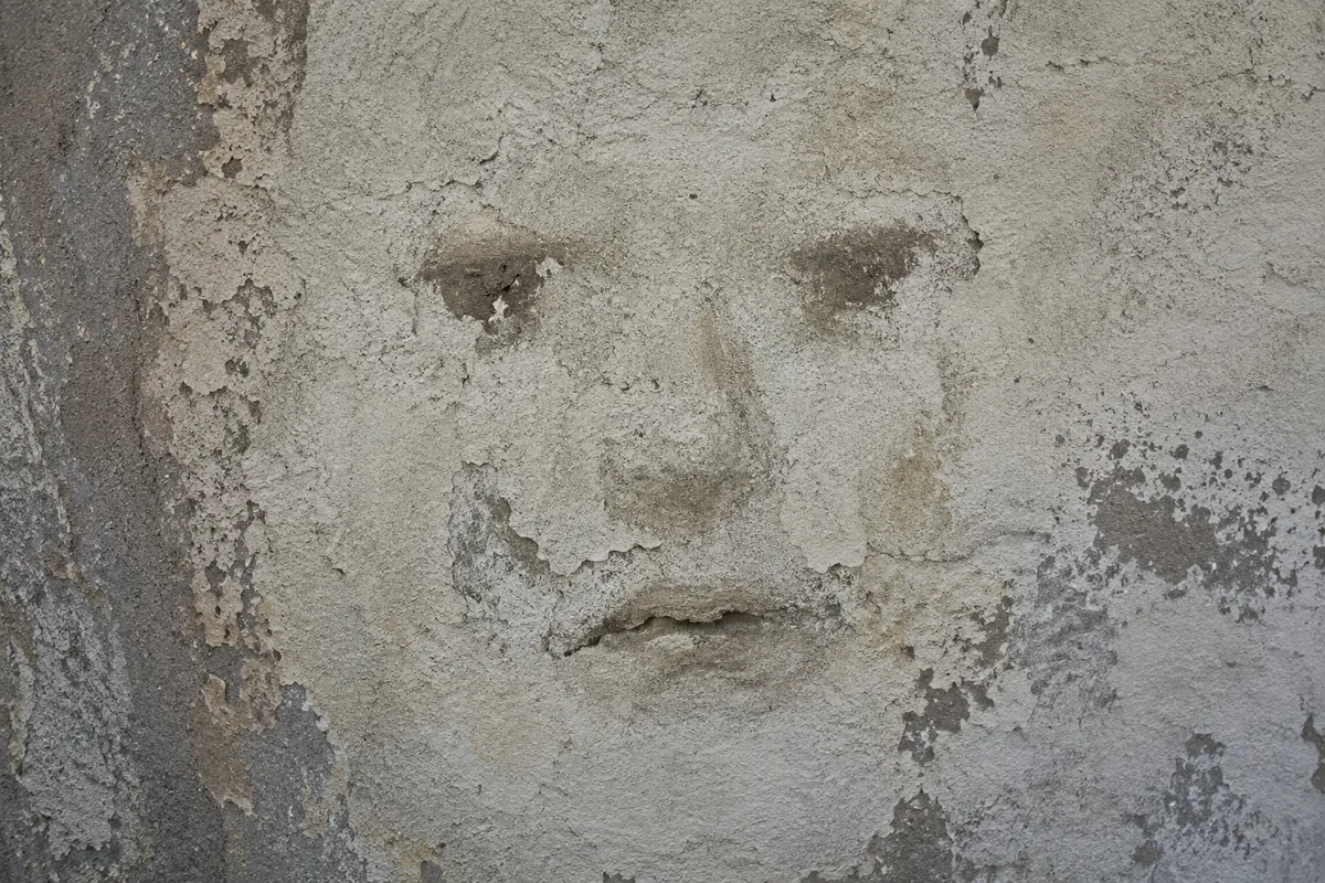 Marks and weathering on an old wall create the illusion of a human face.